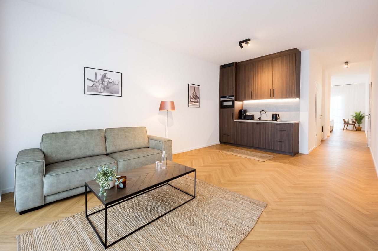 Offener Wohnbereich mit Sofa, Couchtisch und dunkler Küchenzeile auf Fischgrätparkett